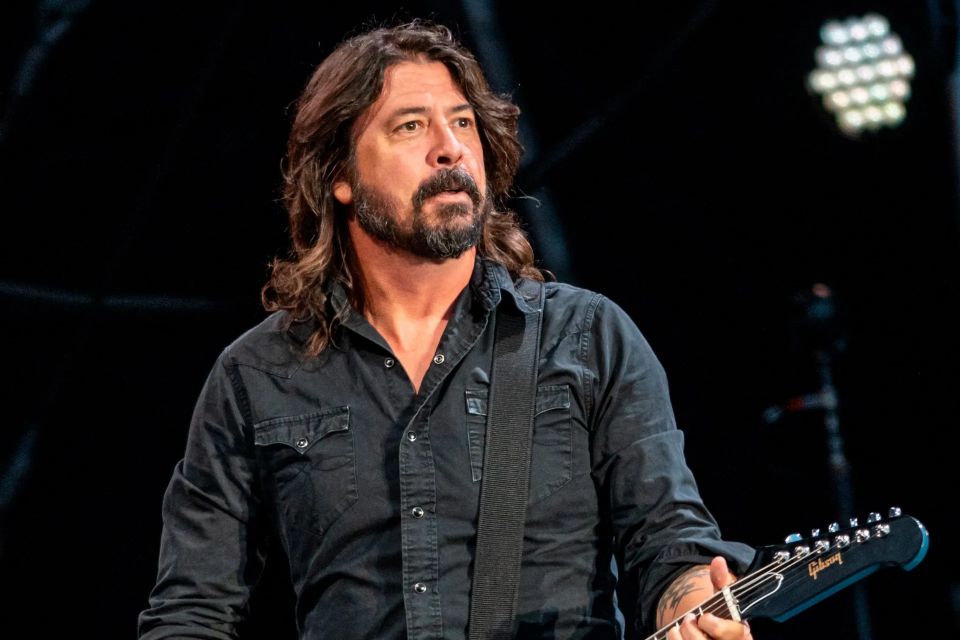 Dave Grohl on stage playing his guitar- image from the waist up 