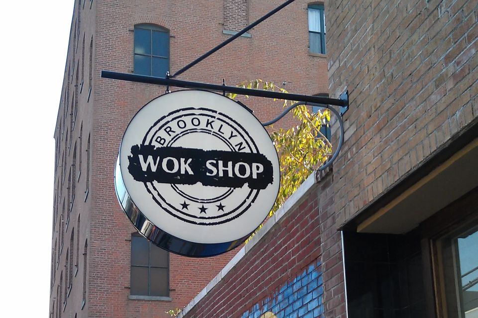 Round white illuminated blade sign with a black circular logo projecting from a brick building on a bracket