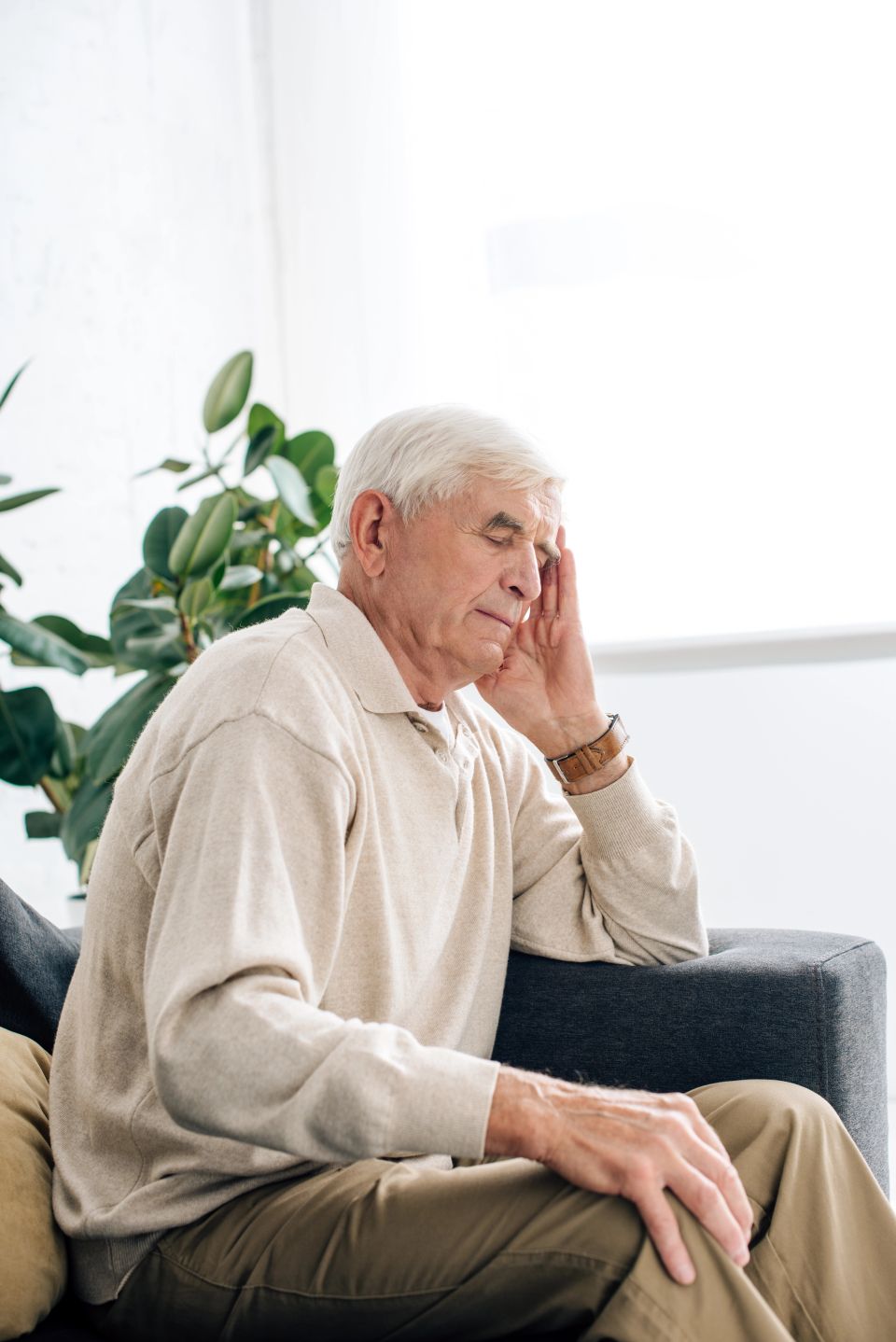 Senior man sitting on sofa and having headache in apartment