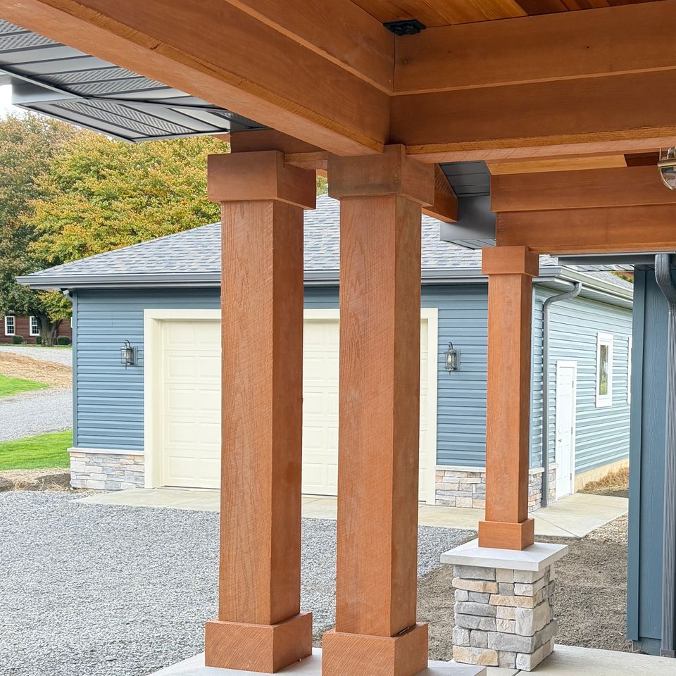 Custom covered outdoor structure featuring wood columns, stone bases, a wood-paneled ceiling, and recessed lighting attached to a residential home.