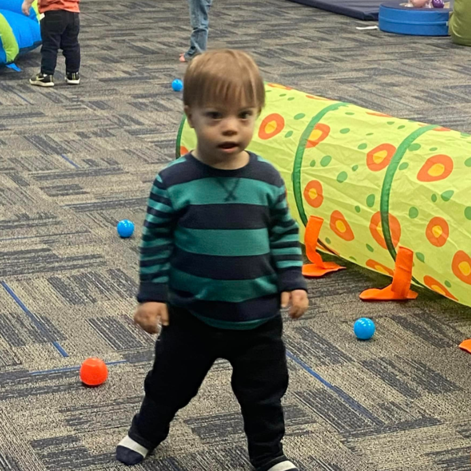 Toddler with Down syndrome exploring an indoor play area during a Down Syndrome Association of the Valley program.