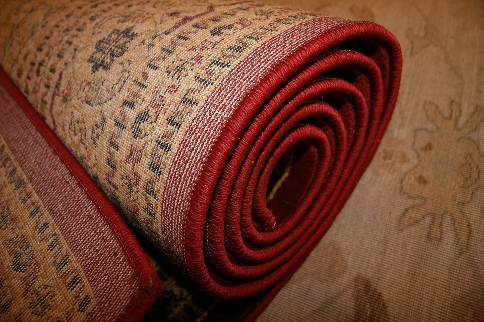 Close-up of rolled-up patterned rug with beige background, red border, and detailed black and red designs