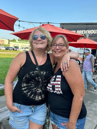 Two women posing together outdoors near event seating and gathering areas.