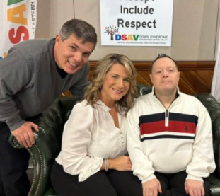 Community members posing with a self-advocate in front of an "Include Respect" sign at a Down Syndrome Association of the Valley event.