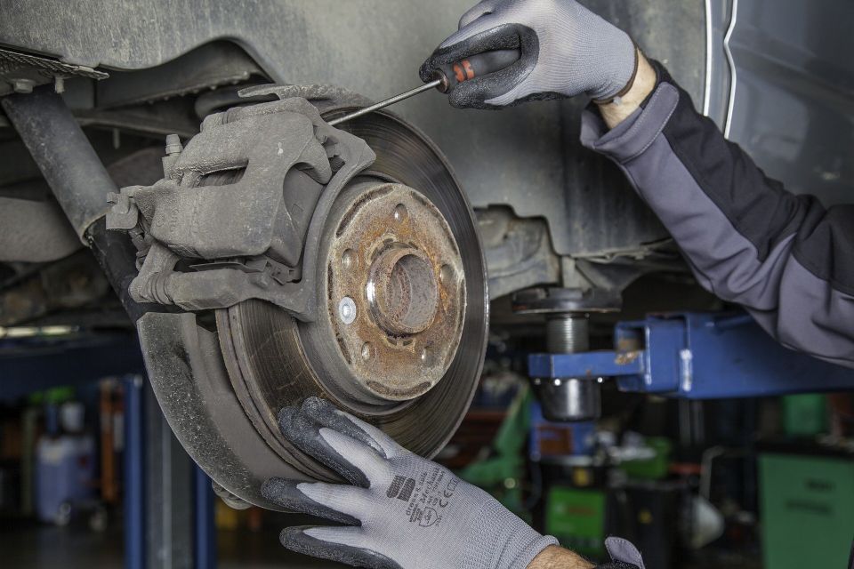 Image of an auto mechanic working on a rear disk brake on the passenger side.