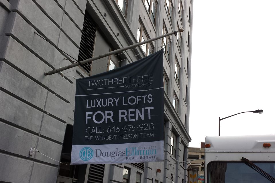 Fabric hanging sign on a long pole bracket with tension cables above a building entrance