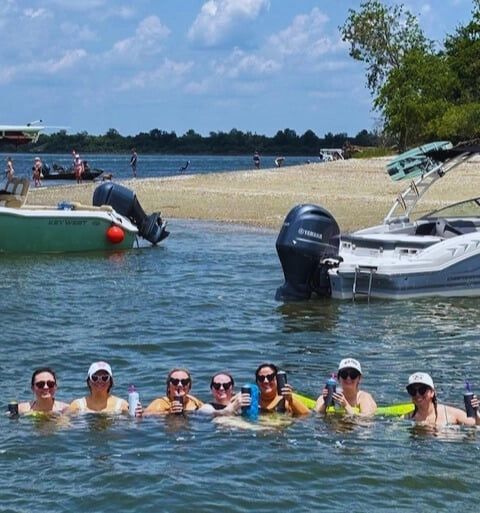 Group of women floating with drinks during a Charleston bachelorette party at a sandbar near the boat
