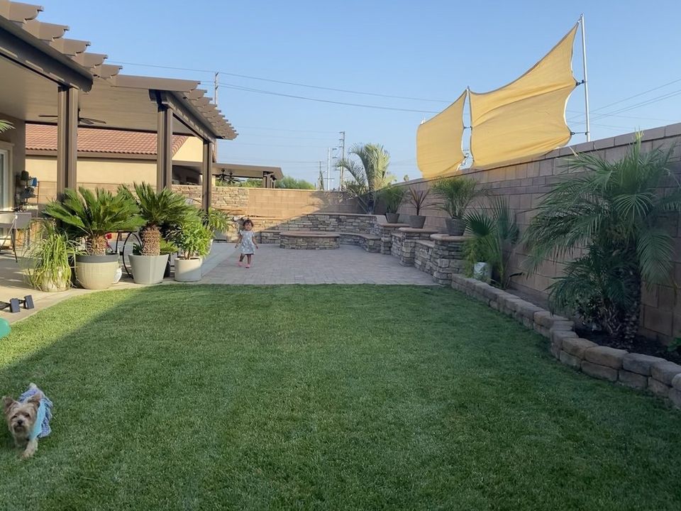 Beautiful backyard renovation with green lawn, retaining wall, decorative landscaping, and outdoor living area