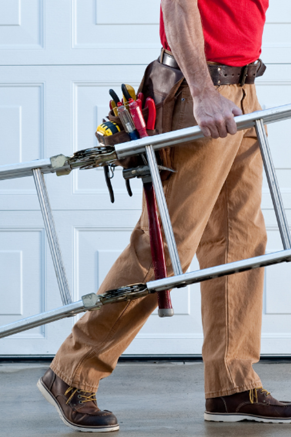 Service technician carrying an extension ladder and tools while arriving at a residential property for professional home maintenance services.