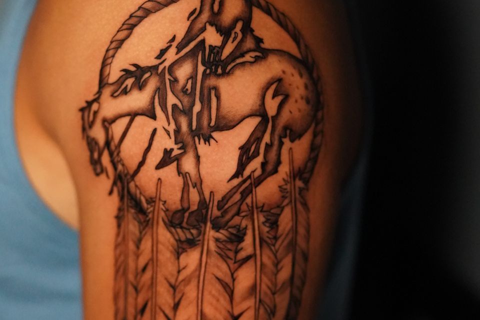 Image of a tattoo on a mans left shoulder depicting the "End of the trail" symbolized by an indian on horseback exhausted from his journey and sleeping on his horse as the horse also sleeps in black and grey ink.