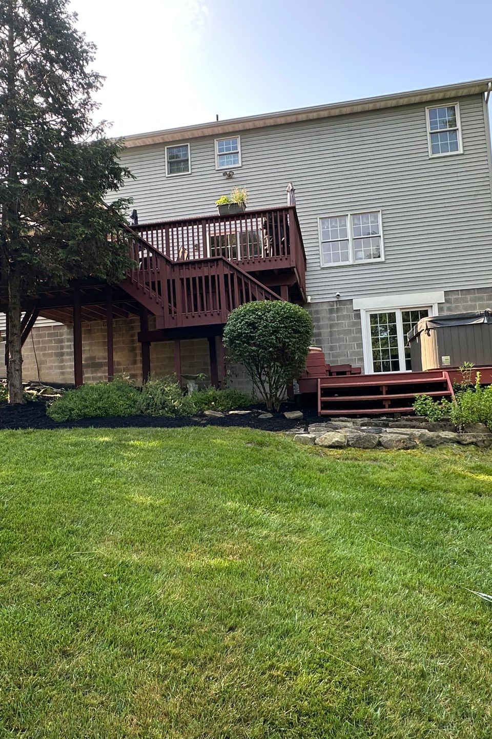 Backyard landscape with a raised deck, hot tub, manicured lawn, mulched planting beds, and trimmed shrubs maintained by R.E.P. Companies.