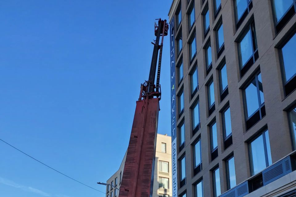 Red boom truck with outriggers down on a Brooklyn street, a vertical banner going up the building behind it