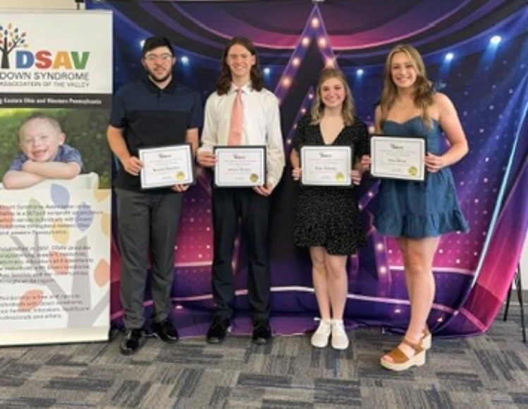 Four scholarship recipients holding certificates while posing at a DSAV recognition event.