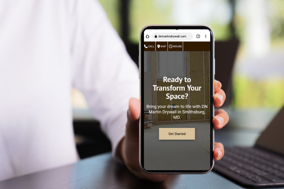 Hand holding smartphone displaying DN Martin Drywall mobile website with call to action for drywall installation services in Smithsburg Maryland.