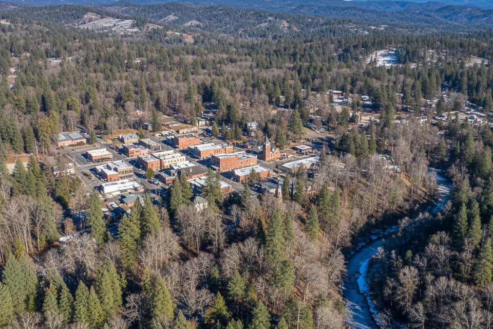 Aerial drone view of historic downtown Grass Valley, CA, showing the dense pine and oak canopy surrounding commercial buildings and Wolf Creek where Lyons Tree Service provides expert care
