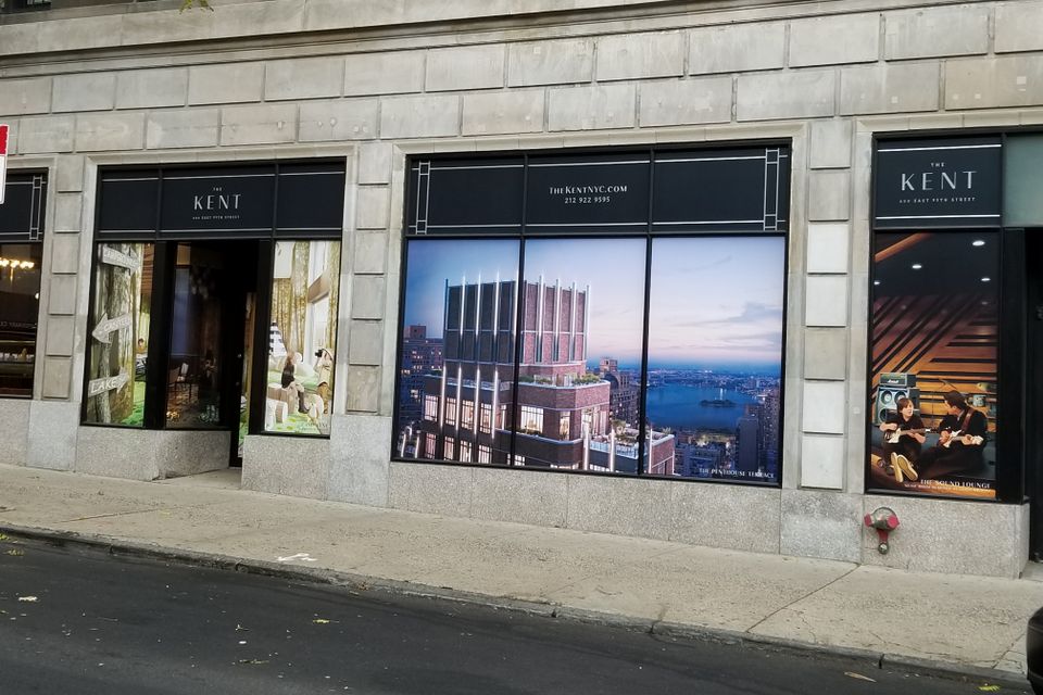 Printed window graphics filling four adjoining storefront windows along a stone building frontage