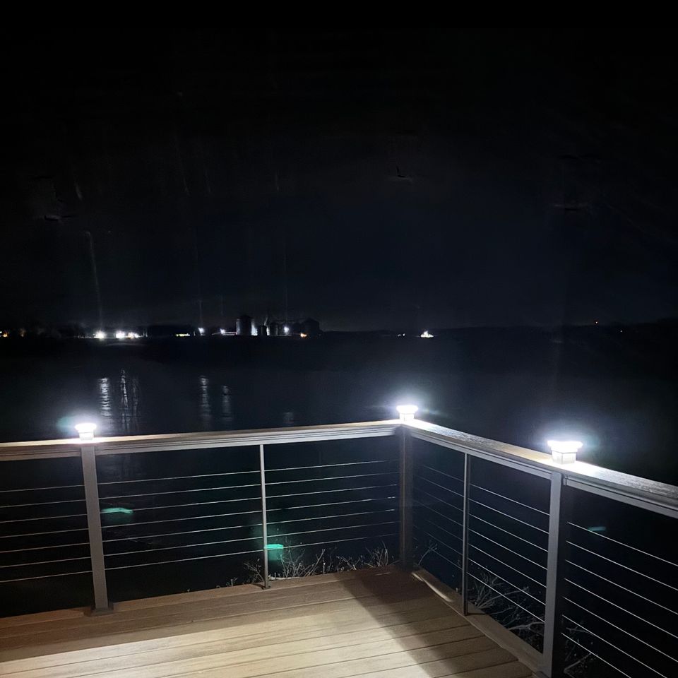 Custom deck overlooking the water featuring cable railings, integrated post lighting, and composite decking at night.