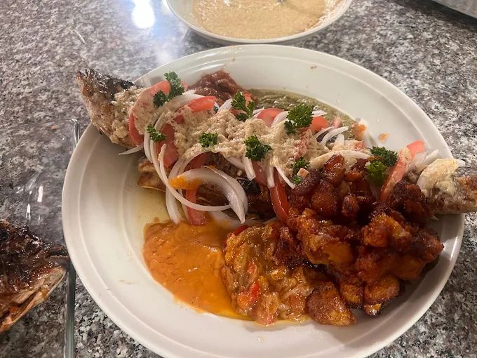 Grilled fish topped with onion and tomato served with fried plantains in sauce at a Los Angeles Cameroonian kitchen