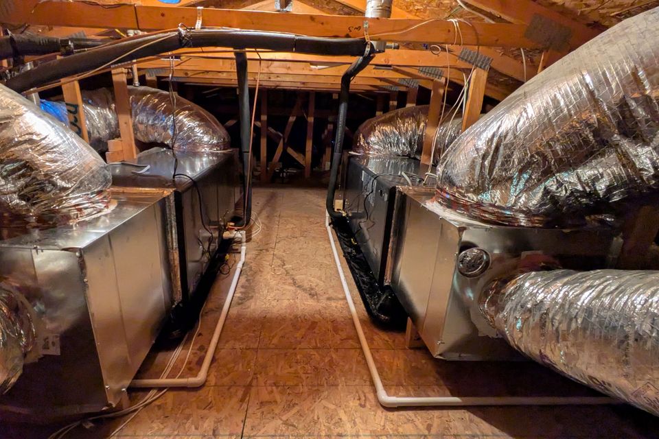 Dual high-efficiency HVAC air handlers installed in an attic with insulated flexible duct-work, organized condensate drain lines, and professionally routed components for residential heating and cooling.