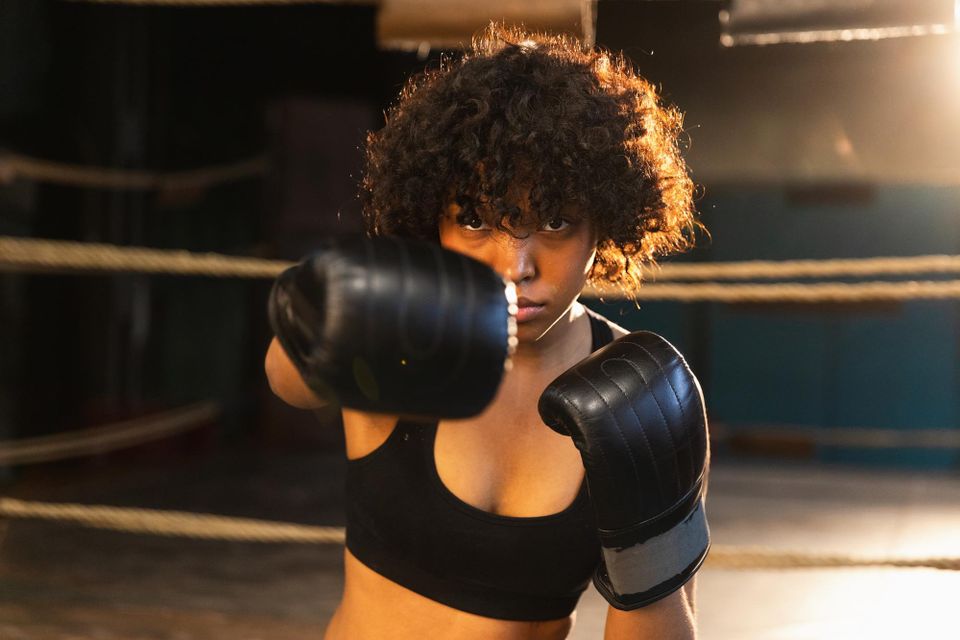 Woman in boxing gloves throwing a jab toward the camera inside a boxing ring