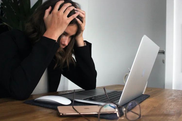 Woman looking at her laptop screen seeming very stressed out or frustrated
