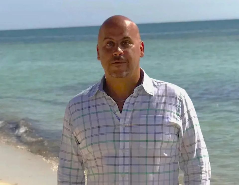 Mike Calvo on a beach, wearing a light-colored checkered with the ocean and clear blue sky in the background.