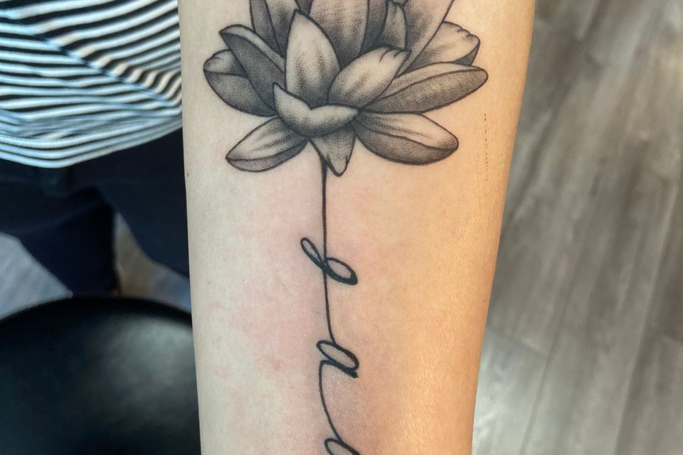 Image of a tattoo of a flower in black and grey with initials