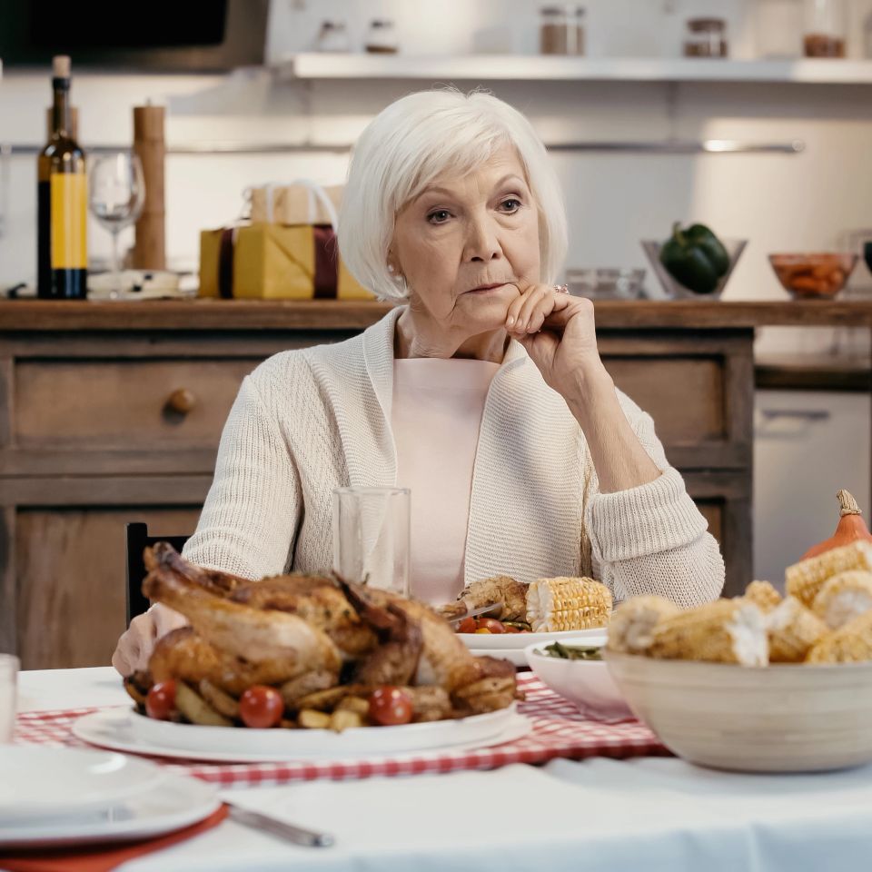 Lonely and thoughtful senior woman sitting near thanksgiving dinner served on table in kitchen