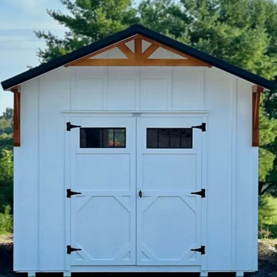 Front view of a white Alpine cottage shed with double barn doors and wood accents