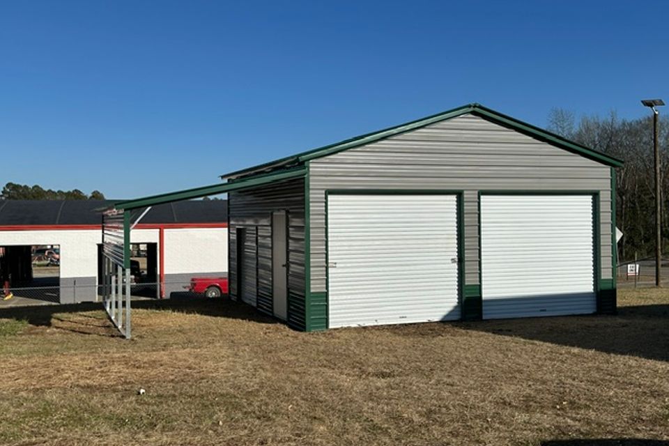 Green and white steel garage with roll up doors and open lean to representing steel garages in Alabama