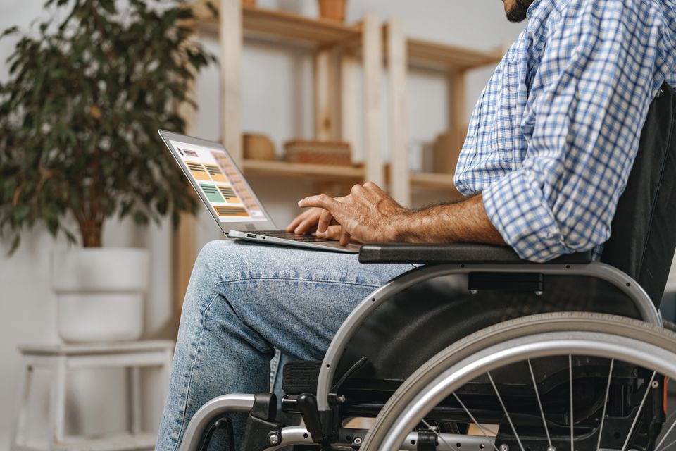 45960474 disabled man sitting in a wheelchair and using laptop