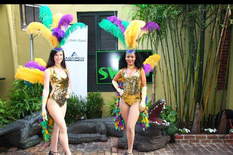 Two showgirls with Mardi Gras colored feathers in the courtyard of The Swamp on Bourbon Street for a corporate event.