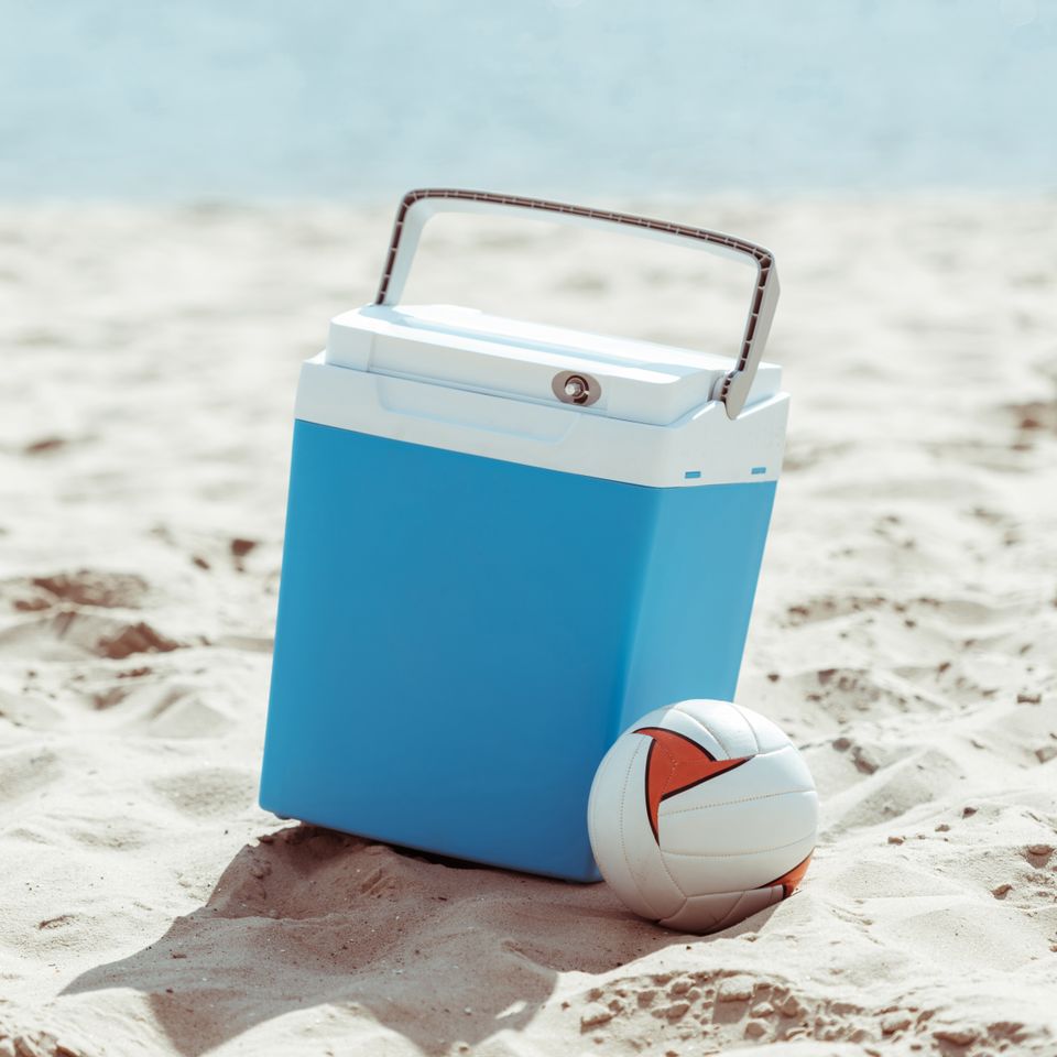 Blue beach cooler and volleyball resting on the sand for beach cooler rentals