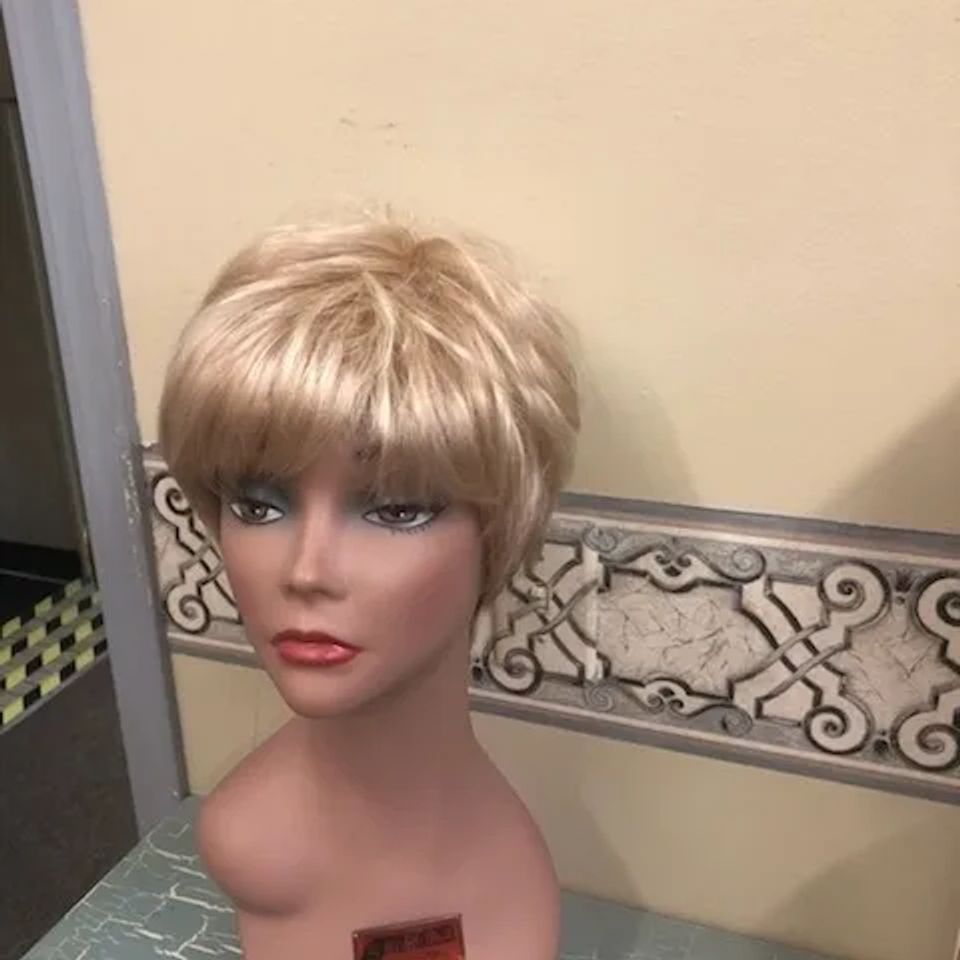 Short blonde layered wig with full bangs displayed on a mannequin at Shears Wigs & Hairpieces Salon.