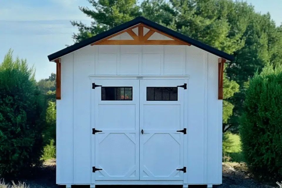 Front view of a white Alpine cottage shed with double barn doors and wood accents