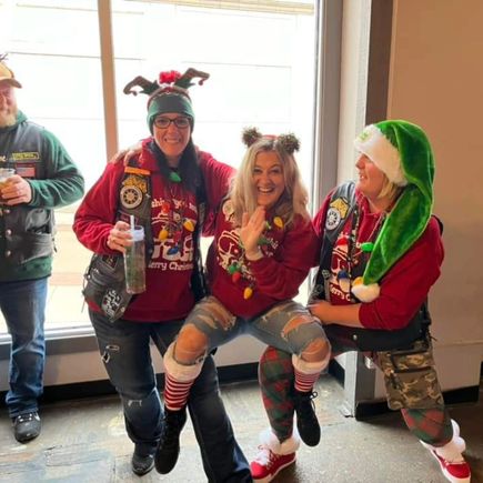 Three attendees wearing holiday-themed clothing and accessories posing together during a Christmas event.