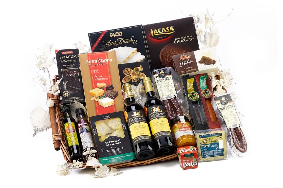 Gourmet gift basket with Spanish wine, olive oil, honey, pâté, cheeses, chocolates, cured meats, anchovies, mushrooms, crackers, truffles, and decorative white flowers. Christmas