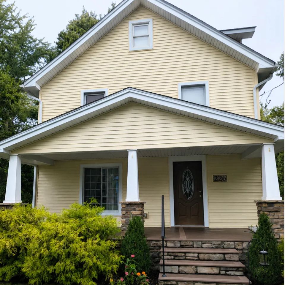 Clean home exterior with light-colored siding, a front porch, stone steps, and landscaped yard.