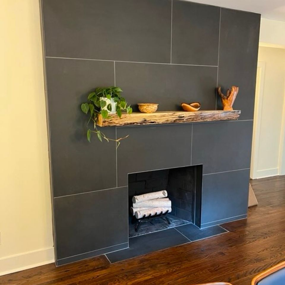 Large format charcoal tile fireplace surround with live edge wood mantel from a living room remodel