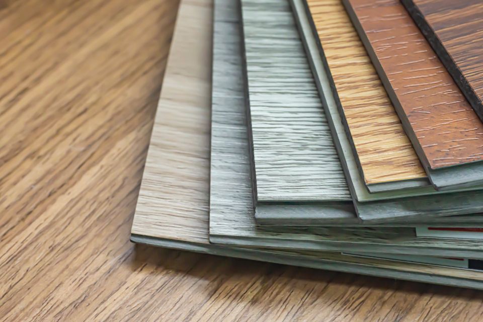 Stack of vinyl plank flooring samples in mixed wood tones on a wood surface
