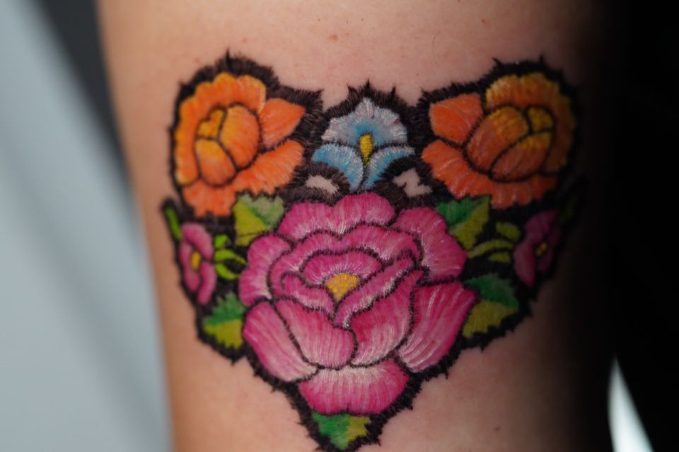 Image of a woman's thigh top just above the knee tattoo in very colorful reds, oranges, yellows, greens in a small cluster