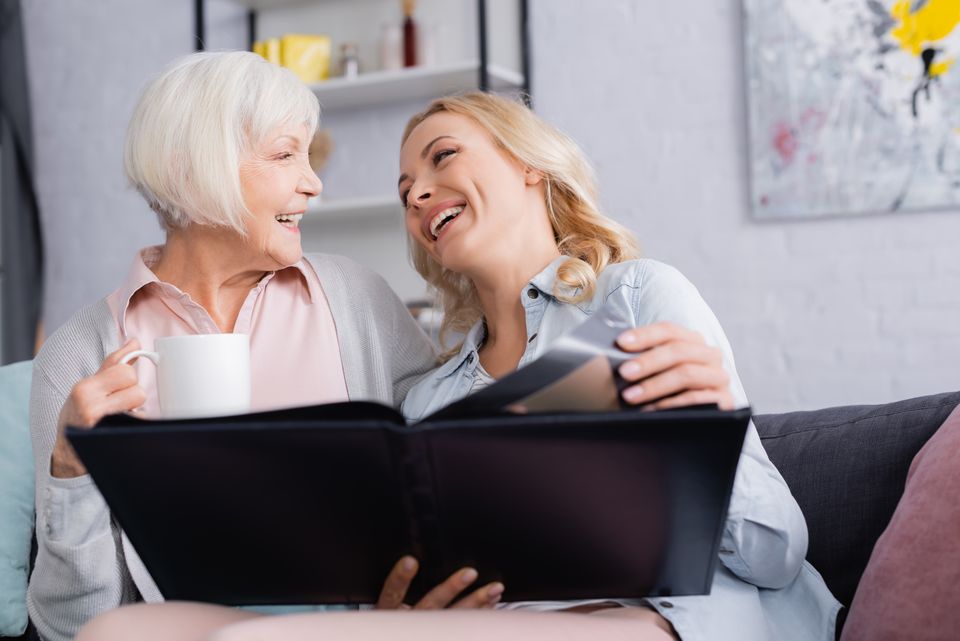 Two women laughing together over a photo album and coffee after Brainstorm vitamin IV therapy