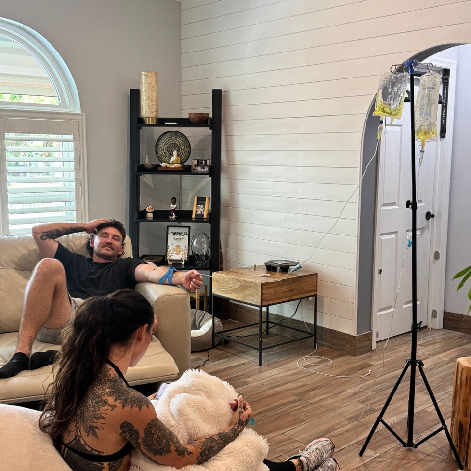 Nurse setting up a mobile IV drip for a man relaxing on a living room couch in Palm Beach County