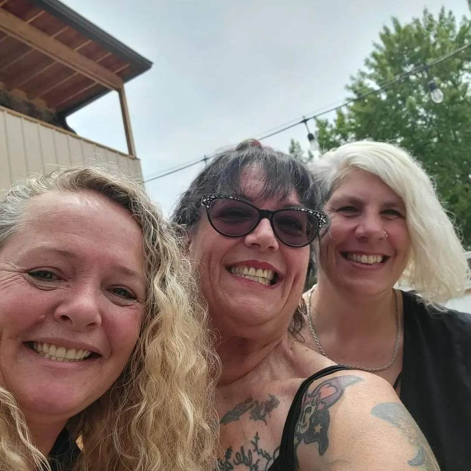Three women smiling for a selfie outdoors during a casual gathering.