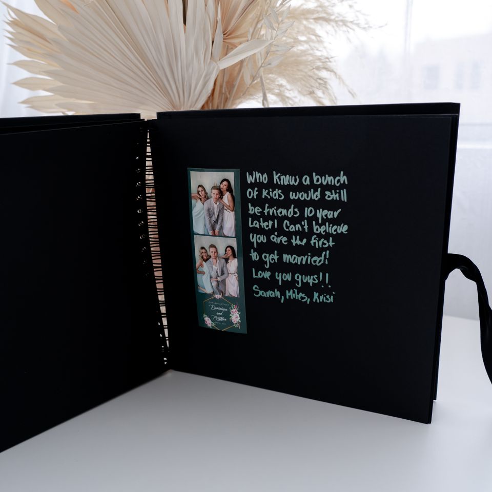Open guestbook with photo booth strip and handwritten message on a black page.