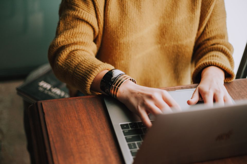 Person wearing a tan sweater and two bracelets is typing on a laptop computer