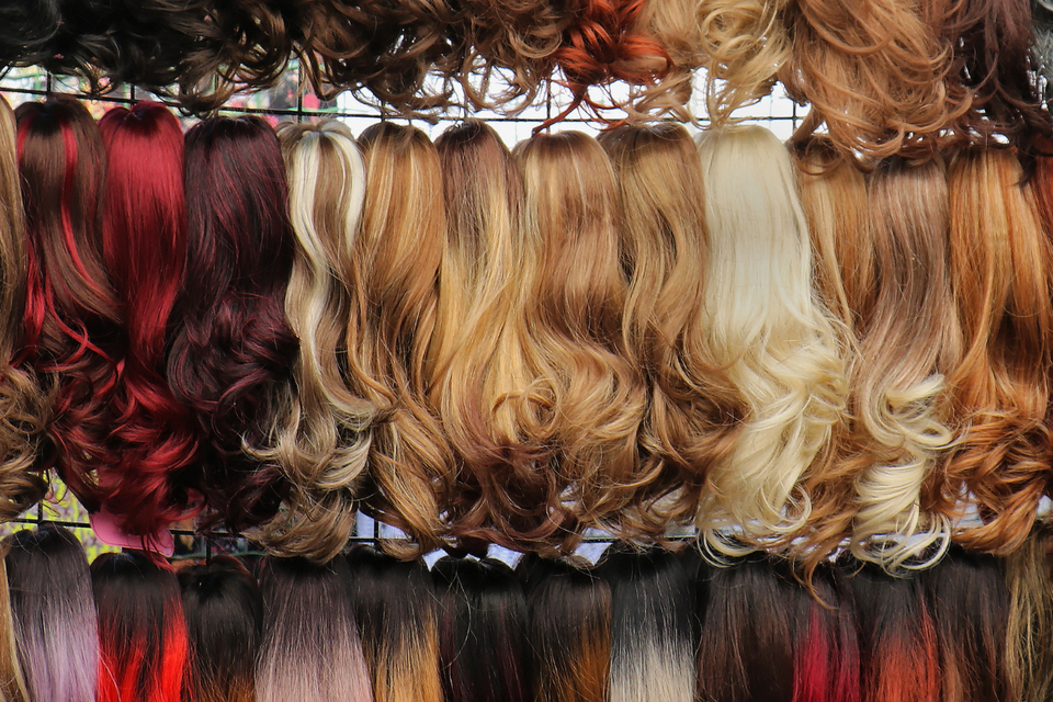 Display of wigs in various colors, lengths, and curled styles hanging on racks inside Shears Wigs & Hairpieces Salon.