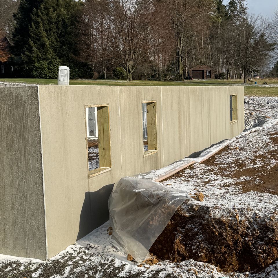 Concrete foundation under construction for a residential home addition with framed window openings and site preparation in progress.