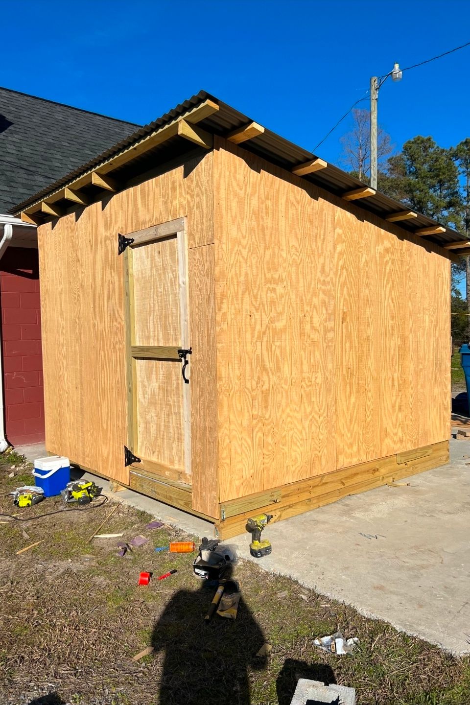 New plywood storage shed with metal roof under construction beside brick building in Virginia Beach VA