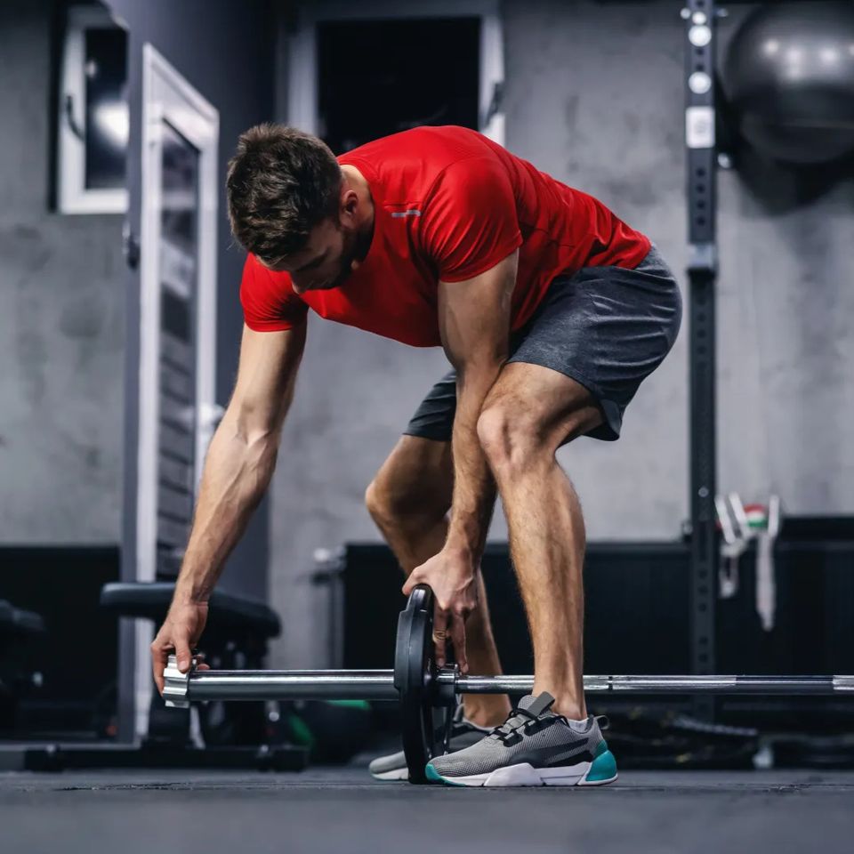 Man in a red shirt loading a barbell in a gym before Recovery and Performance IV therapy in Palm Beach County